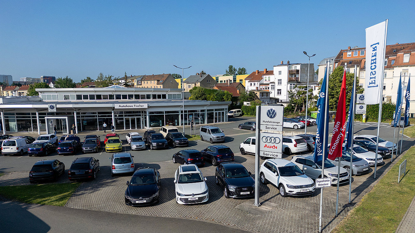 Autohaus Fischer Gera – Außenansicht des Volkswagen, Audi und VW Nutzfahrzeuge Standorts mit Service-Beschilderung, Fahnen und Fahrzeugbestand auf dem Parkplatz.